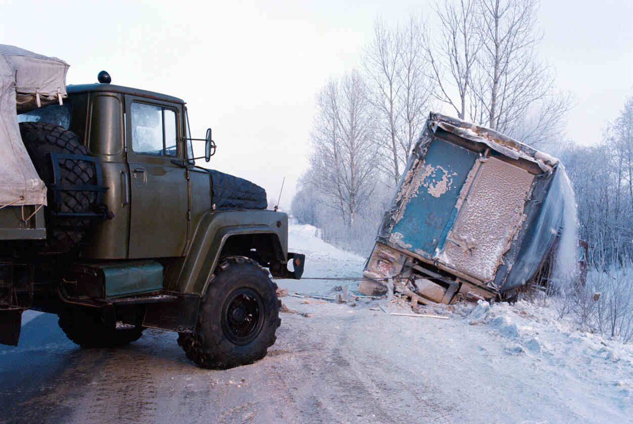 Delivery truck accident on icy snowy road in Colorado showing truck towing damaged trailer after crash